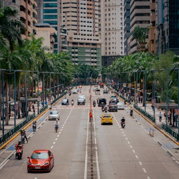 A vibrant street scene in Manila, Philippines with cars, motorbikes, and tall buildings lined with palm trees.